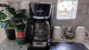 Una cocina con cafetera, una planta en maceta y una taza sobre la encimera.