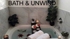 Un baño con bañera, un letrero que dice 'BATH & UNWIND' y plantas decorativas.
