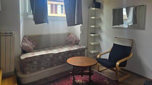 A living room with a sofa, a chair, a small table, a radiator, a window with curtains, and a mirror on the wall. - Steps to Duomo: Historic Florence Studio (Florence)