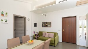 Ein modernes Wohnzimmer mit einem grünen Sofa, einem Esstisch mit Stühlen und einer Holztür.