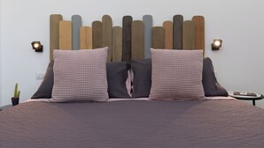 Ein Bett mit einem Kopfteil aus Holzbrettern, zwei karierte Kissen, einer dunklen Decke und zwei Wandleuchten.