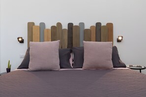Ein Bett mit einem Kopfteil aus Holzbrettern, zwei karierte Kissen, einer dunklen Decke und zwei Wandleuchten.