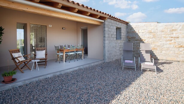 Eine überdachte Terrasse im Freien mit Esstisch und Stühlen, einer Steinsäule und Kiesboden.