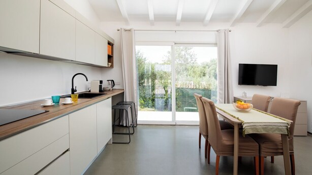 A modern kitchen with white cabinets, a wooden countertop, and a sliding glass door leading to a balcony.