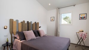 A neatly arranged bedroom with a bed, a small table with a cactus, and a window with curtains.