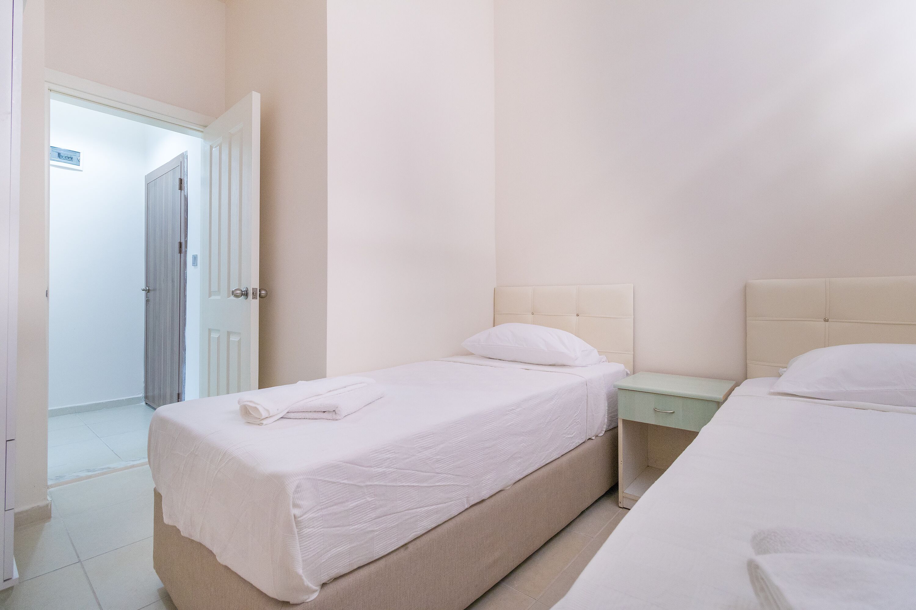 A bedroom with two beds, a nightstand, and a door leading to another room.