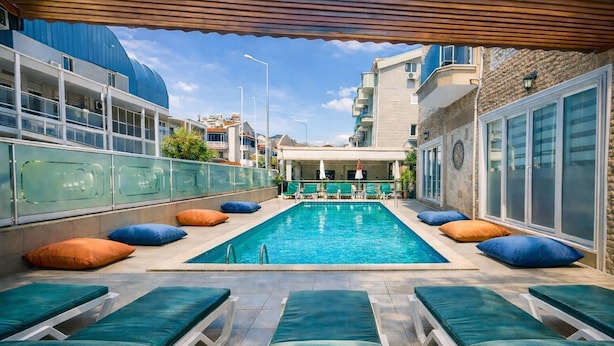 A swimming pool with lounge chairs and umbrellas, surrounded by buildings. - STAR APART OTEL MARMARİS  (Marmaris)
