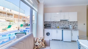 A modern kitchen with a washing machine, a dining area with a table and chairs, and a view of a pool and building outside. - STAR APART OTEL MARMARİS  (Marmaris)