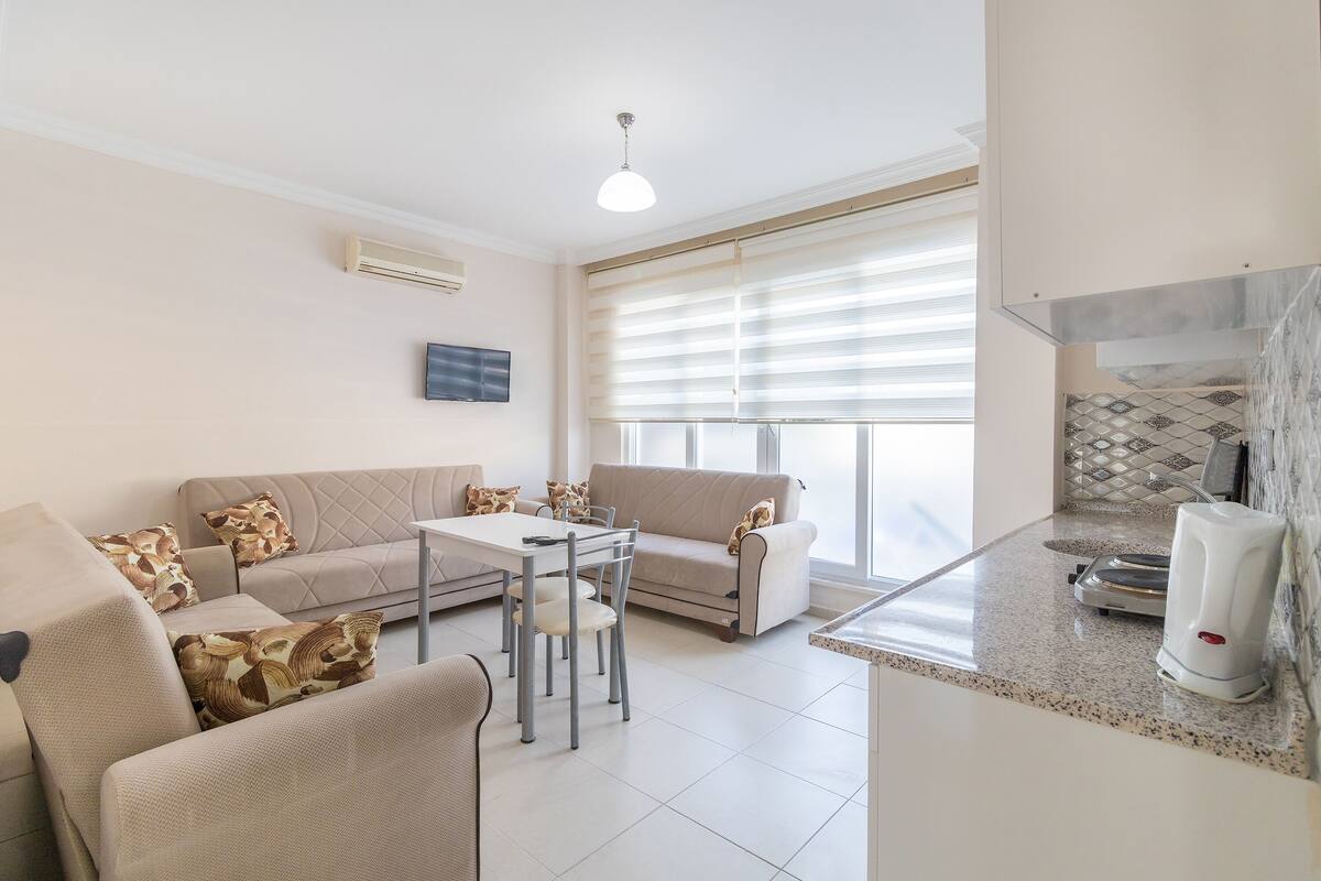 A modern living room with a sofa, chairs, a dining table, and a kitchen area with a toaster.