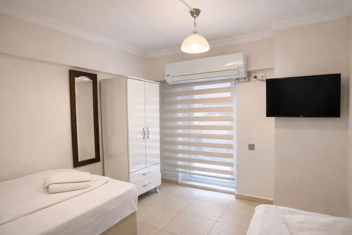 A bedroom with a bed, a wardrobe, a television, and a window with blinds.