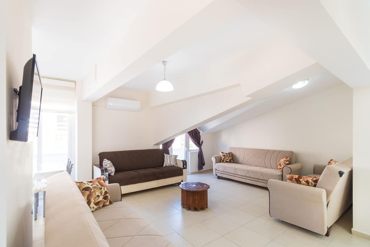 A spacious living room with a high ceiling, two sofas, a coffee table, and a flat-screen TV mounted on the wall.
