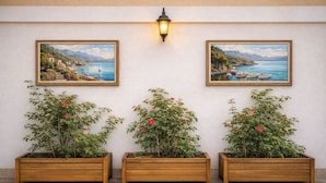 Three wooden planters with plants and flowers against a wall with two framed paintings. - STAR APART OTEL MARMARİS  (Marmaris)