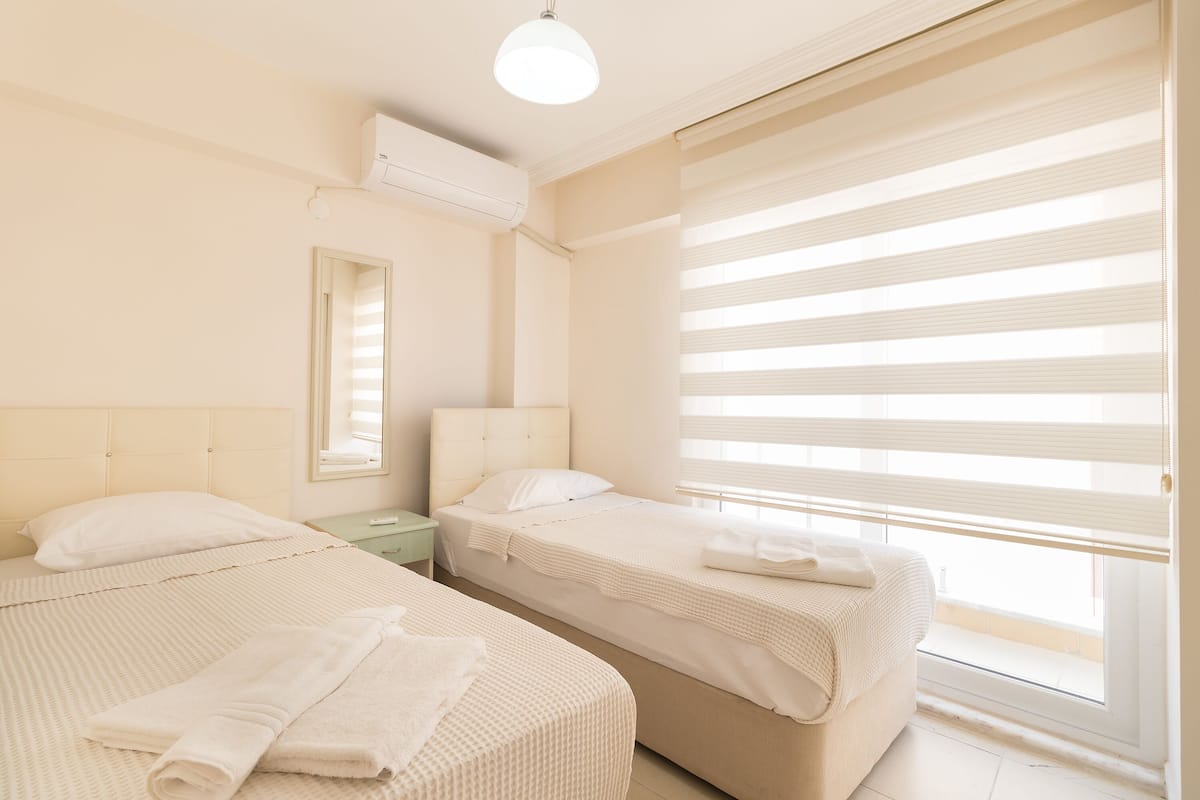A hotel room with two beds, a nightstand, a mirror, and a window with blinds.