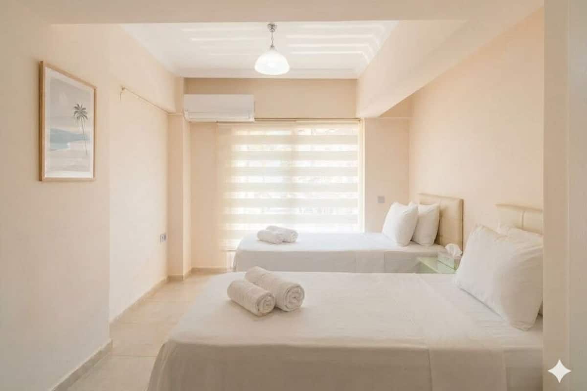A hotel room with two beds, a ceiling fan, a framed picture on the wall, and a window with blinds.