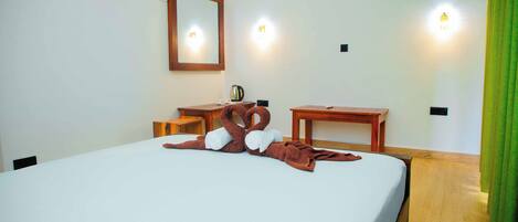 Habitación de hotel con una cama bien tendida, un escritorio de madera, una silla, un espejo y una pequeña mesa con una tetera.