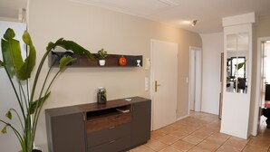 Un saló modern amb un moble fosc de fusta, una planta verda gran i una estanteria amb objectes decoratius.