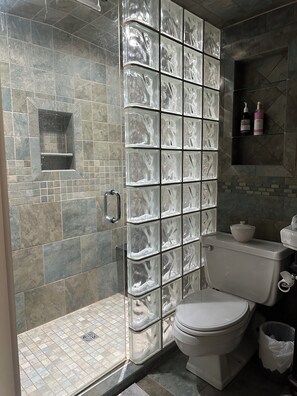 A bathroom with a glass shower enclosure, a toilet, and a sink.