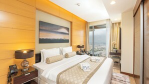 A hotel room with a large bed, two bedside tables with lamps, a painting on the wall, a desk with a chair, and a view of the city through the window. - PVH - 1BR - Emaar Fashion Avenue (Dubai)