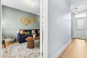 Un salon avec un canapé bleu, une table basse en bois et des œuvres d’art décoratives accrochées au mur.