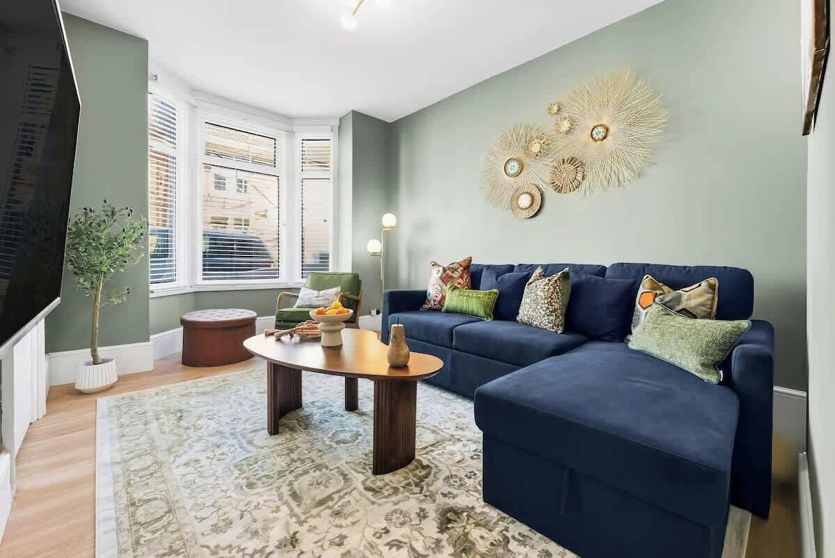 Ein Wohnzimmer mit einem blauen Sofa, einem runden Couchtisch, einer Topfpflanze und einem Wandbild.