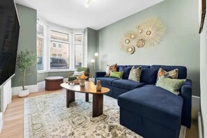 A living room with a blue sofa, a round coffee table, a potted plant, and a wall decor piece.