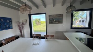 A modern kitchen with a large island, wooden chairs, a hanging light fixture, and a view of the outdoors. - In a haven of peace, charming house, 5 minutes from white sandy beaches (Plounéour-Brignogan-plages)