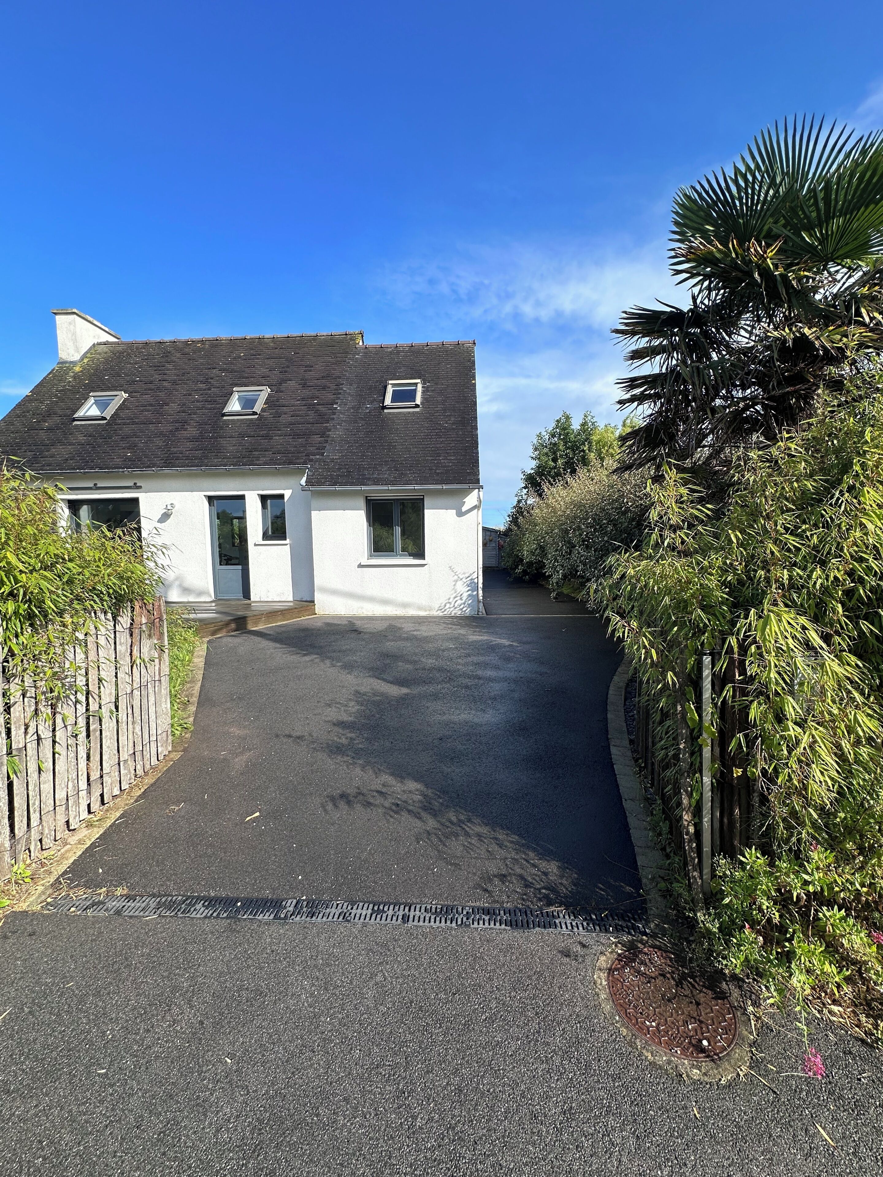Une maison à deux étages, avec un toit sombre, des murs blancs et une allée pavée.