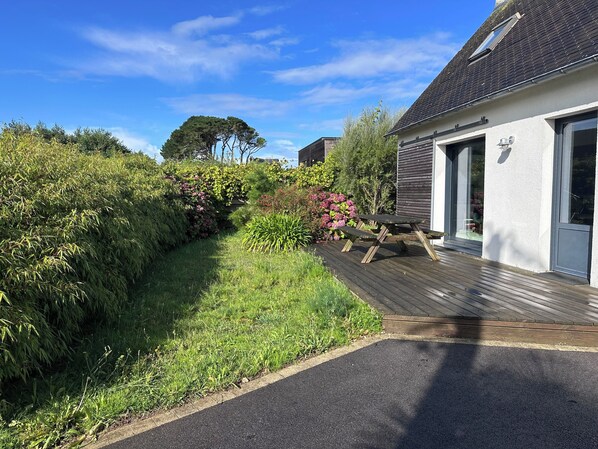 A residential property with a wooden deck, a white exterior wall, and a garden with various plants and flowers. - In a haven of peace, charming house, 5 minutes from white sandy beaches (Plounéour-Brignogan-plages)