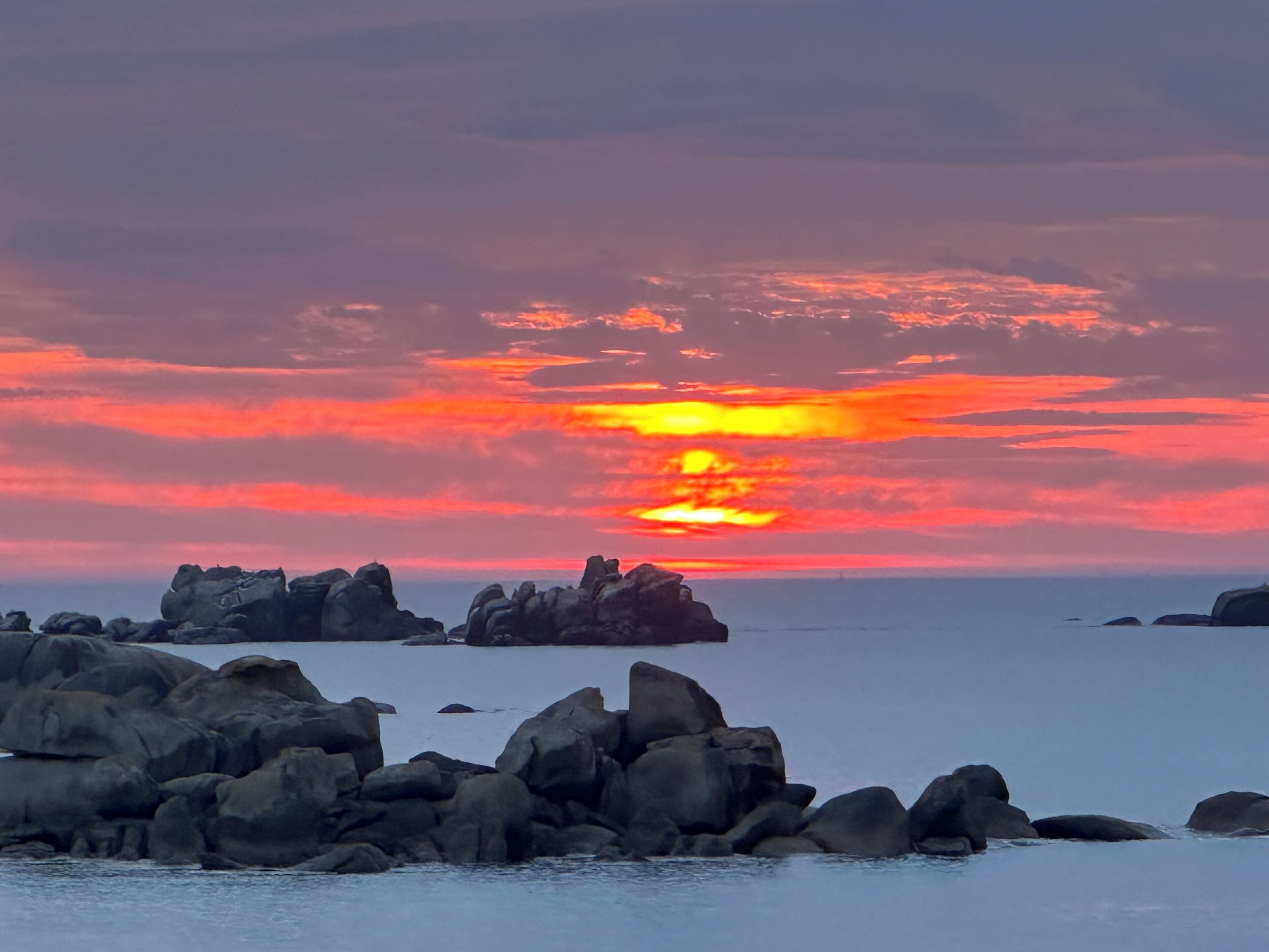 Un atardecer sobre una costa rocosa con grandes rocas en primer plano.