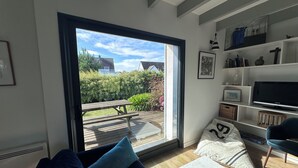 A modern living room with a large sliding glass door leading to an outdoor patio. - In a haven of peace, charming house, 5 minutes from white sandy beaches (Plounéour-Brignogan-plages)