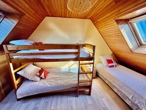 A cozy attic bedroom with a bunk bed and a single bed, wooden walls, and a skylight. - In a haven of peace, charming house, 5 minutes from white sandy beaches (Plounéour-Brignogan-plages)