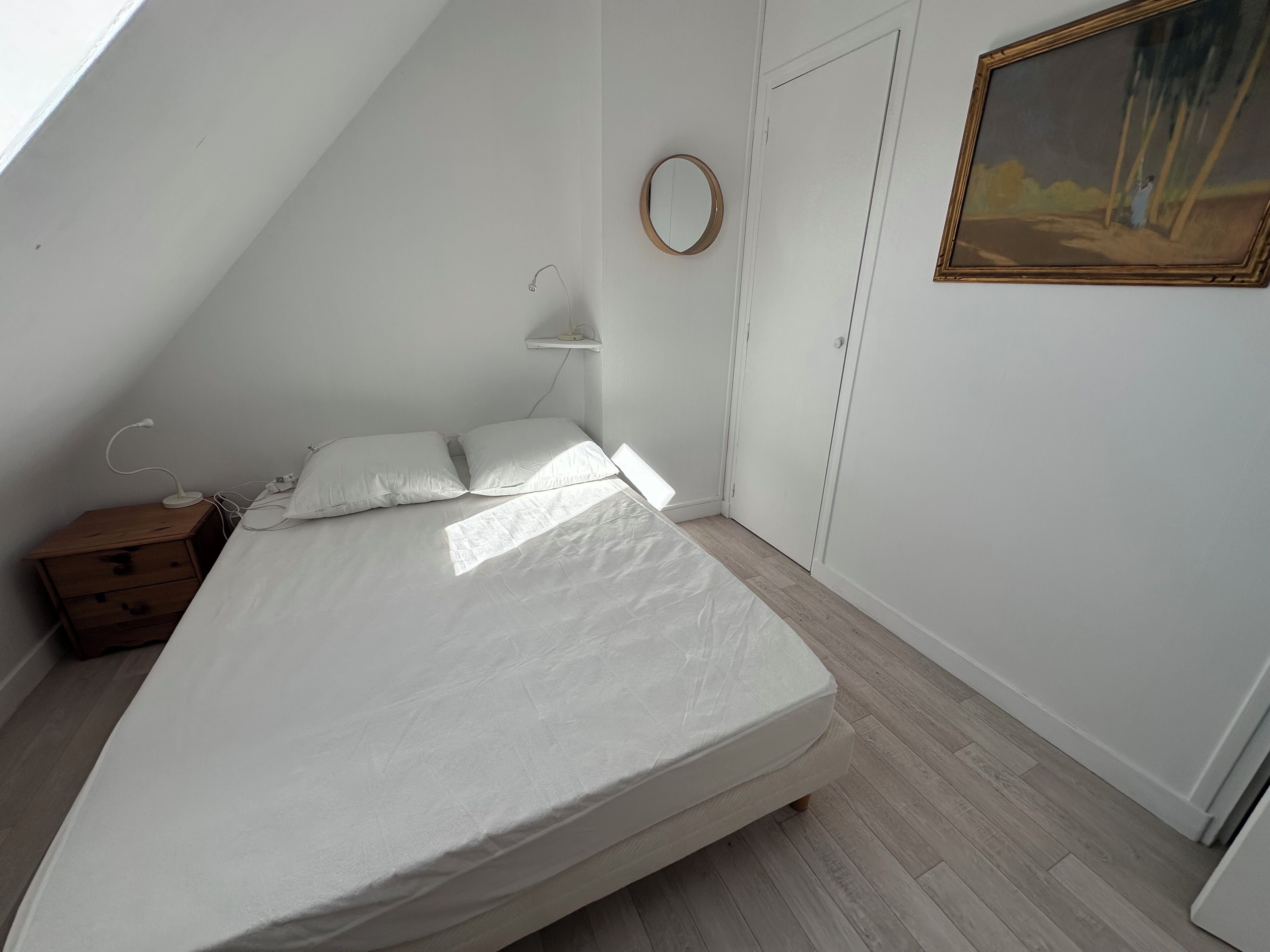 A bedroom with a bed, a bedside table, a lamp, a mirror, and a painting on the wall.