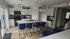 Una cocina moderna con armarios blancos, una isla central con taburetes y una estufa negra.