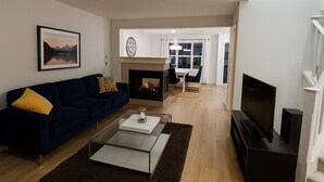 Una sala de estar con un sofá azul oscuro, una mesa de centro de vidrio, una chimenea y un televisor.