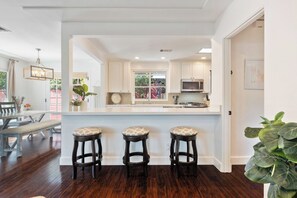 Una cocina moderna con armarios blancos, una isla grande con taburetes y vistas al exterior.