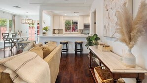 A modern kitchen with white cabinets, a central island, and a dining area with a sofa and chairs. - Charming Coastal Retreat in the Heart of OB! Close to the Beach and Seaworld! (San Diego)