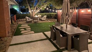 A patio with a wooden table and chairs, surrounded by a brick wall and a hedge. - Charming Coastal Retreat in the Heart of OB! Close to the Beach and Seaworld! (San Diego)