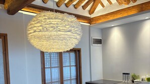 Une salle de conférence équipée d’une table ronde, de chaises, d’un luminaire suspendu, de poutres en bois, d’une fenêtre avec stores et d’un coin kitchenette.