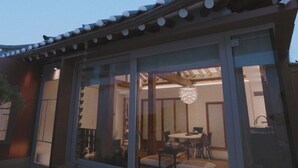 Un bâtiment de style japonais traditionnel, doté de portes coulissantes, d’un coin repas avec une table et des chaises, et d’un luminaire suspendu.