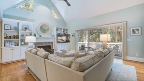 A spacious living room with a large sofa, a fireplace, and a balcony with outdoor seating.