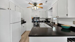 A modern kitchen with white cabinetry, a black countertop, and a ceiling fan. - The Captains Deck, Steps to Beach, Family Friendly (Folly Beach)