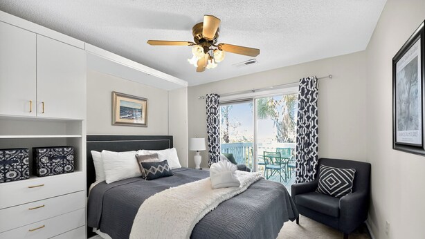 A bedroom with a bed, a ceiling fan, a nightstand, a chair, and a window with curtains. - The Captains Deck, Steps to Beach, Family Friendly (Folly Beach)