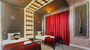 A hotel room with two beds, red curtains, a broom, and a brick wall.