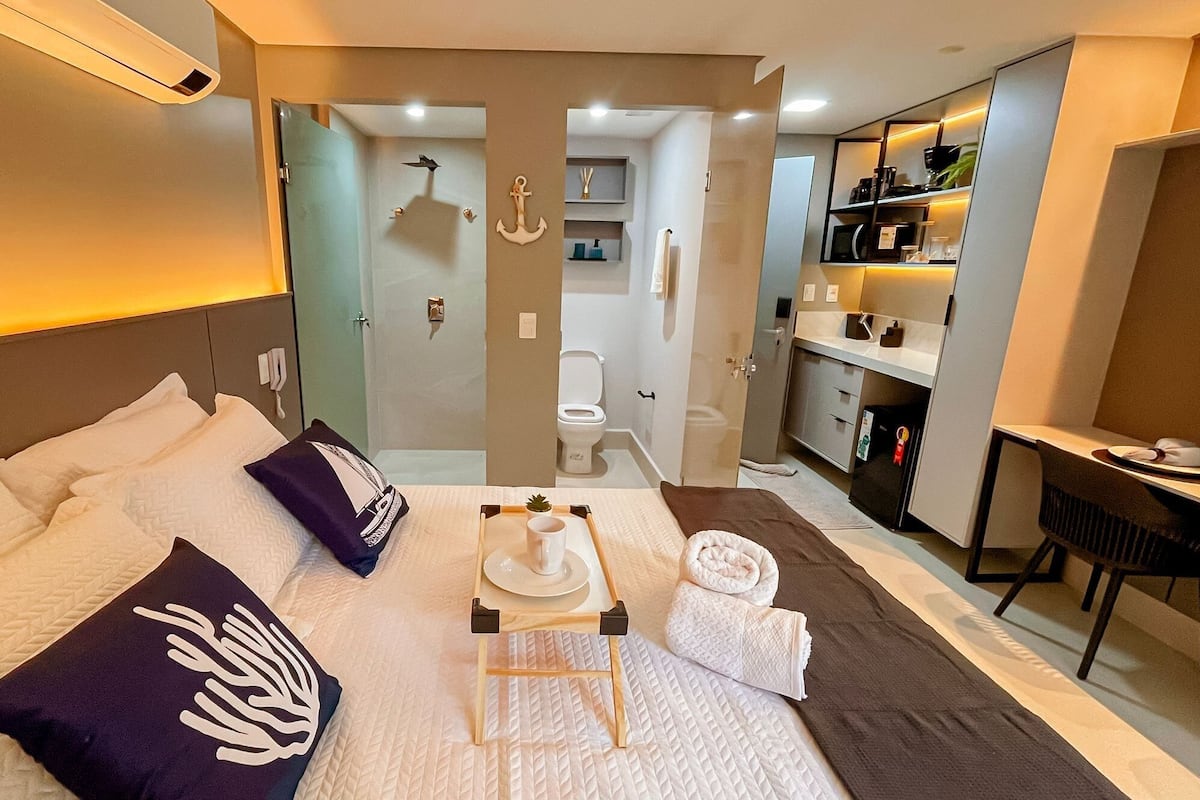 Une chambre d’hôtel avec un lit, une petite table avec un plateau, un bureau et une salle de bain visible à travers une porte ouverte.