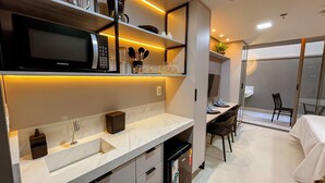 Een moderne keuken met een ingebouwde magnetron, een spoelbak en een koelkast. Er is een eethoek met een tafel en stoelen.