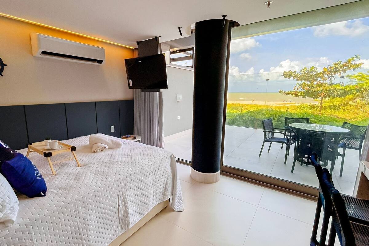Une chambre d’hôtel équipée d’un lit, d’un climatiseur fixé au mur, d’une télévision et d’un balcon avec des sièges pour l’extérieur.