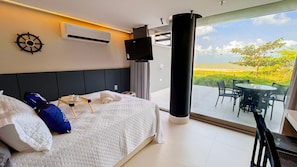 Habitación de hotel con cama, aire acondicionado instalado, televisor y balcón con mobiliario exterior.