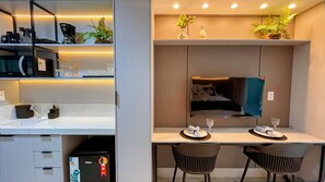 Habitación de hotel moderna con kitchenette, comedor para dos personas, un espejo grande y una cama con vistas.