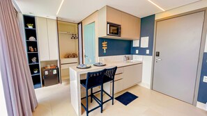 Una kitchenette compacta con microondas, un refrigerador pequeño y una zona de comedor con una silla y una mesa.