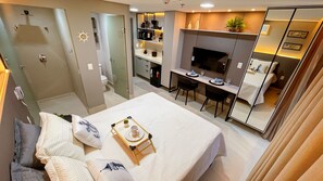 Una habitación de hotel con cama, escritorio, televisor y una pequeña kitchenette.